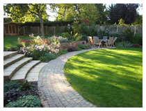 Patio, lawn, path, and steps to upper garden.  Planting includes roses, anemones and grasses.