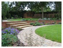 Curving paths run beside a large lawn. Steps rise to shaded garden around the willow tree, and play area under the oak tree.  Garden design in Harpenden, Hertfordshire.