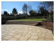 Lower patio, newly completed, paved in random rectangle pattern.  Winter flowering cherry trees are in bloom in this Hertfordshire garden.